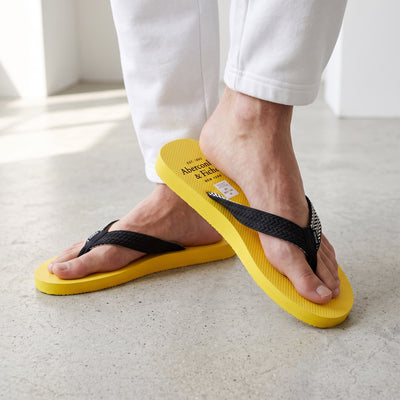 Abercrombie & Fitch yellow flip flops with black straps on model's feet