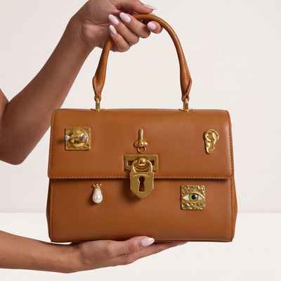 tan top-handle bag with gold decorative hardware held by model