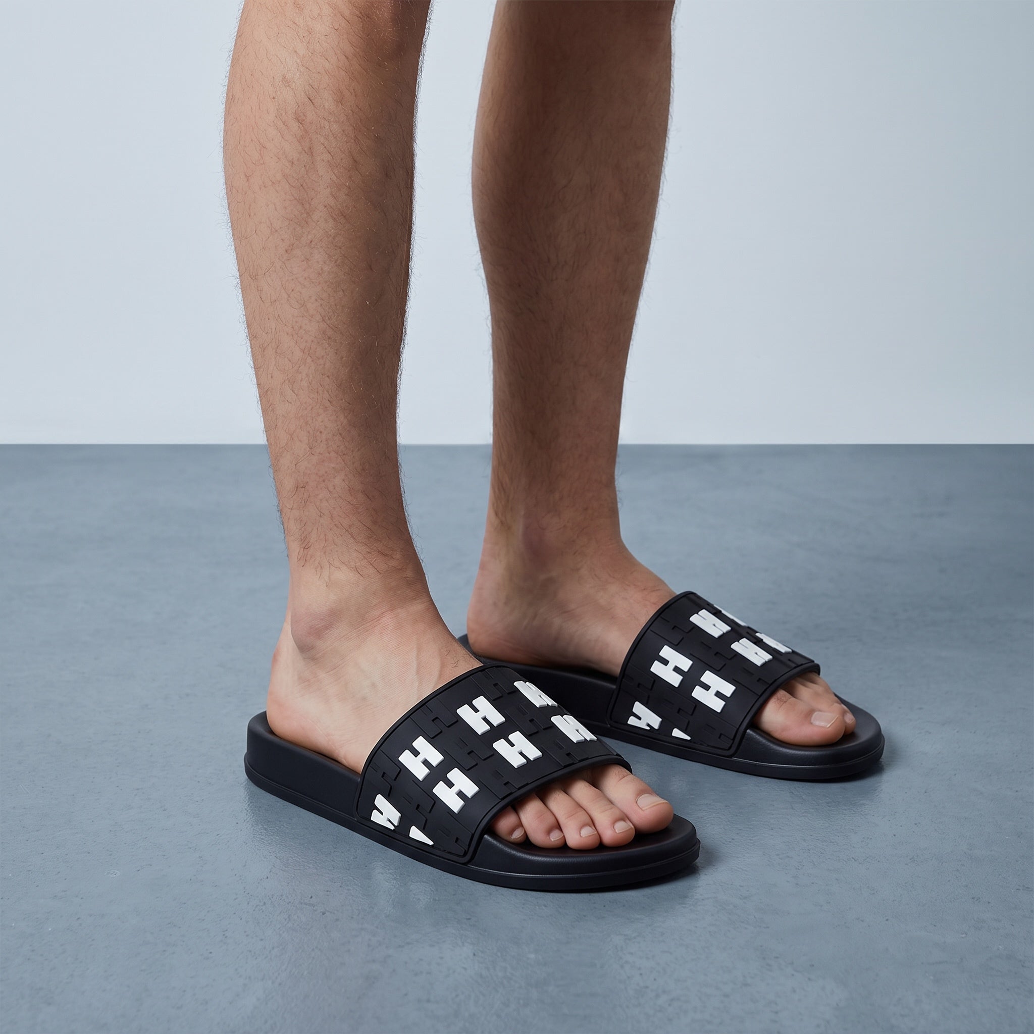 black slide sandals with repeated H logo on strap