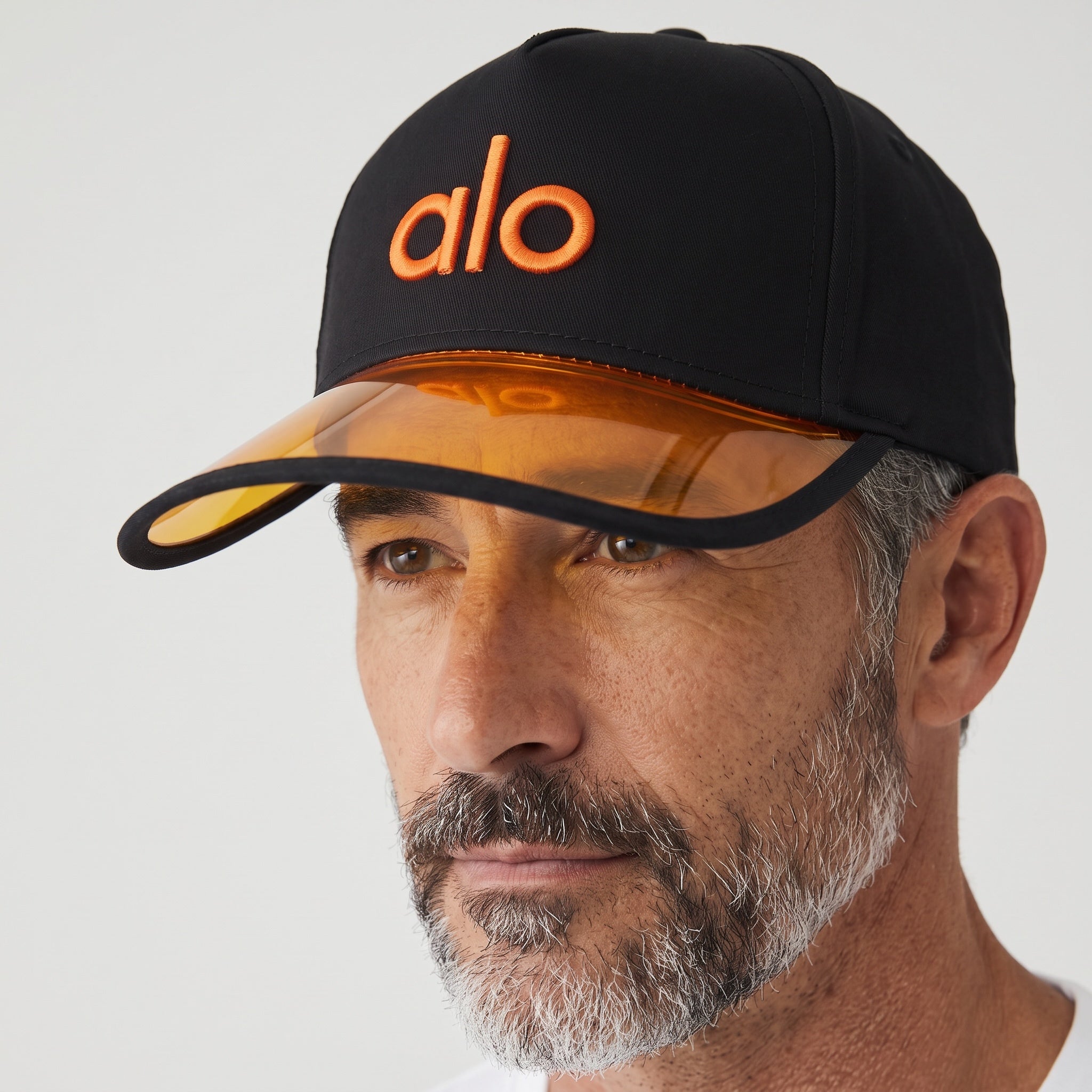 Black baseball cap with translucent orange brim and embroidered Alo logo