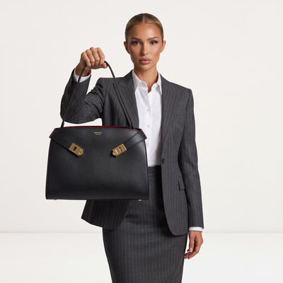 Ferragamo black structured top-handle bag with gold hardware held by model