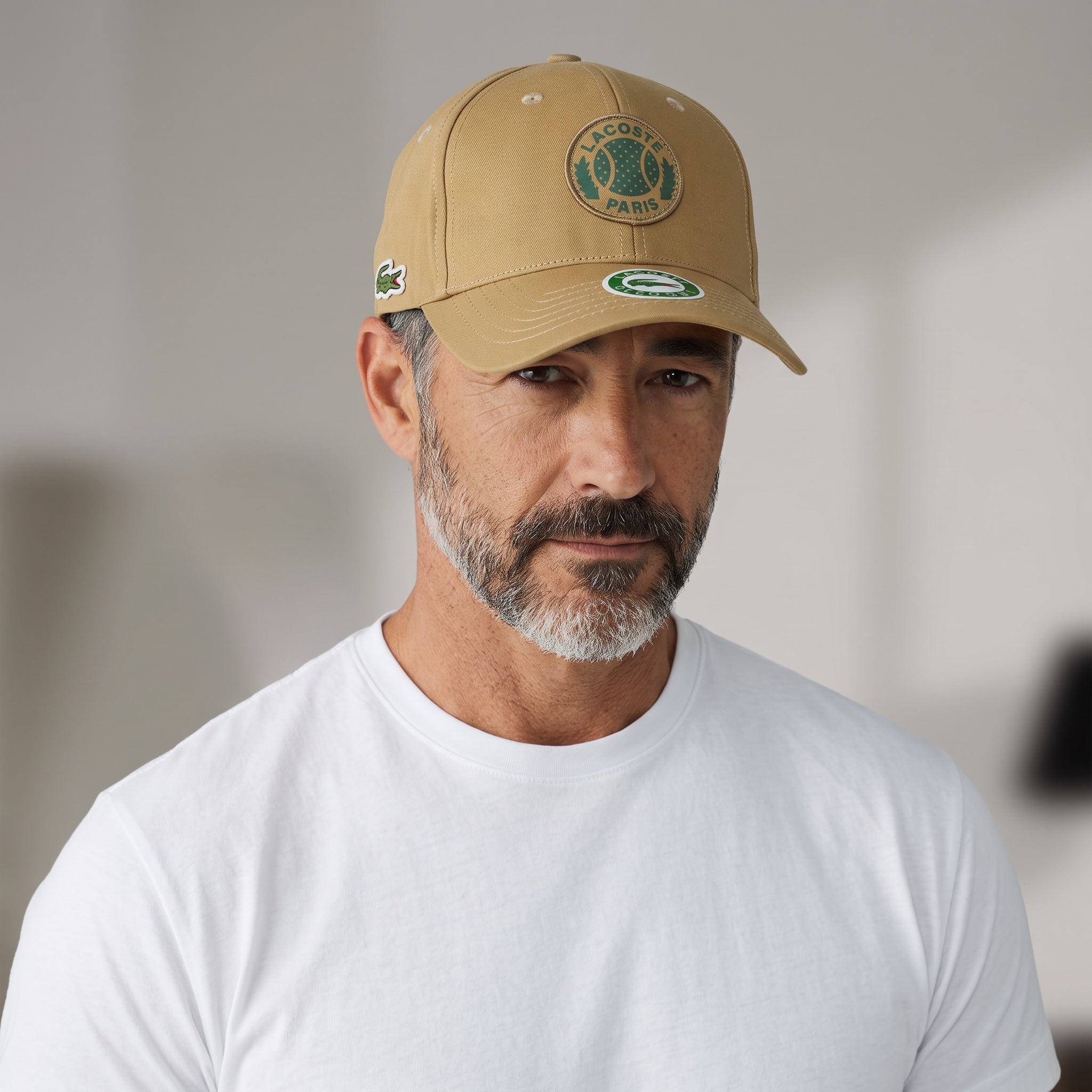 Man wearing a khaki Lacoste Paris baseball cap with tennis ball patch and croc logo
