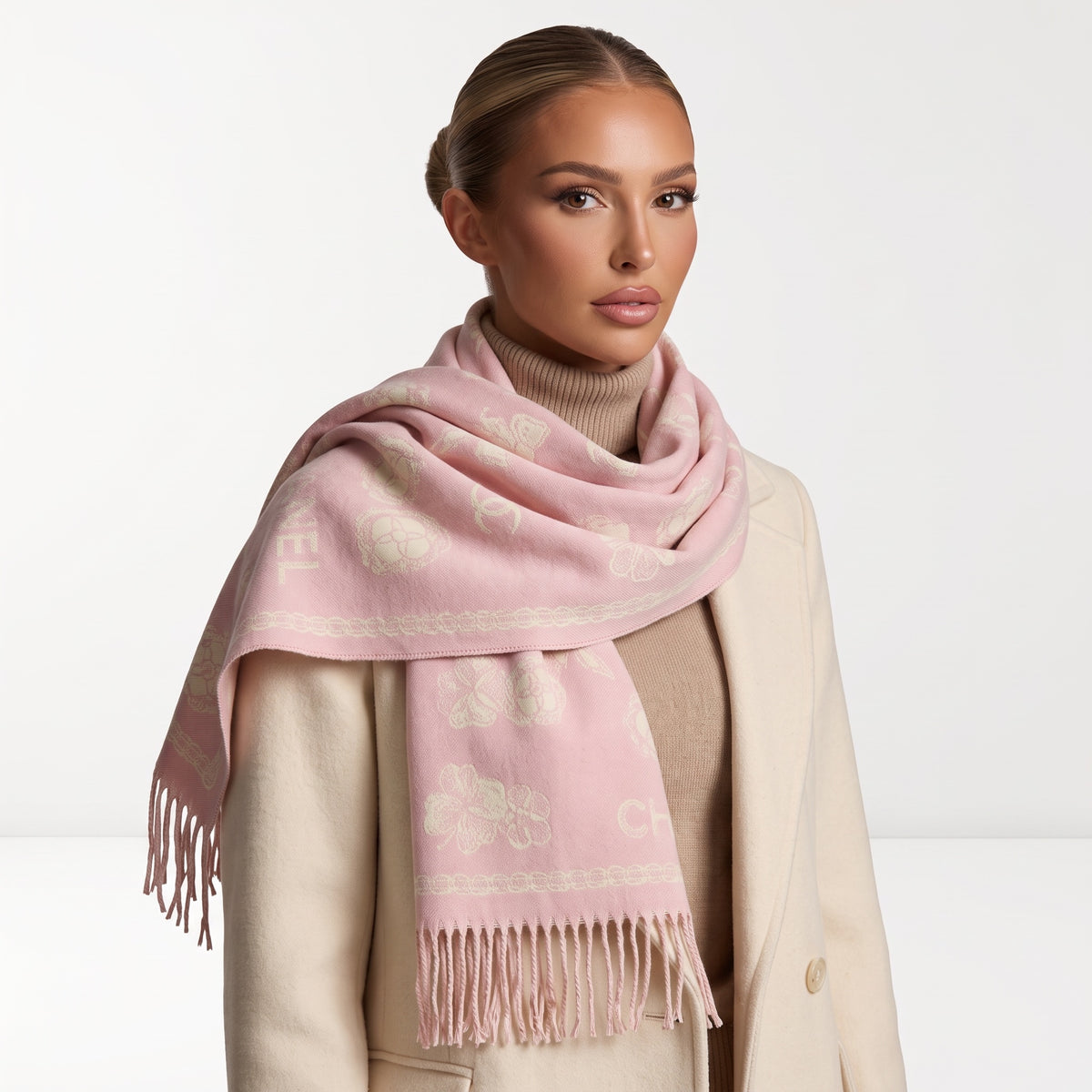 Pale pink Chanel scarf with repeated logo and camellia motifs and long fringe, draped over coat