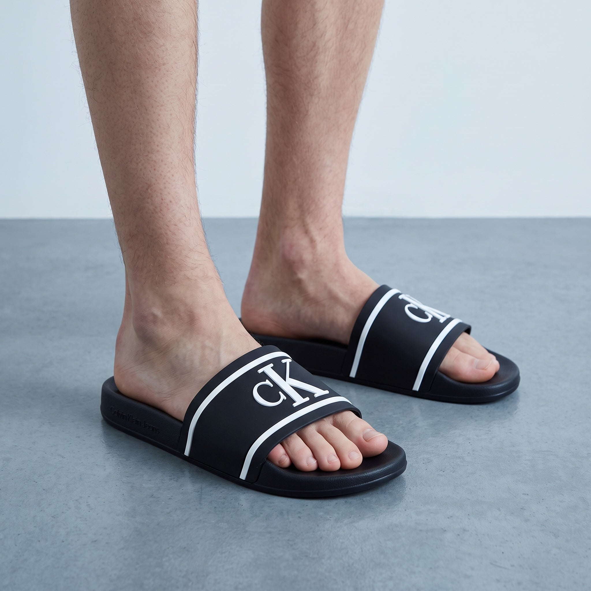 Black Calvin Klein slide sandals with white CK logo on single-band strap