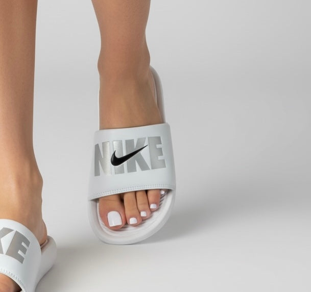 White Nike slides with silver NIKE logo and black Swoosh, cushioned footbed