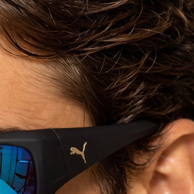 Close-up of man wearing black Puma wrap sunglasses with blue mirrored lenses