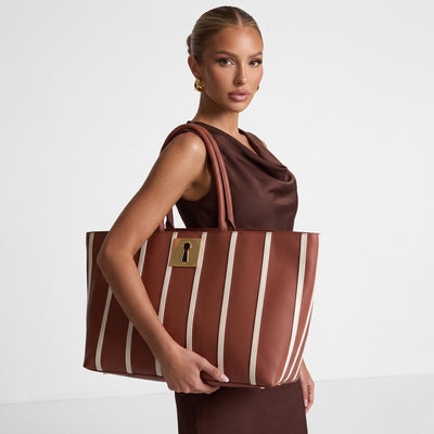 Brown Schiaparelli tote bag with white vertical stripes and gold keyhole plaque, shown with rolled top handles