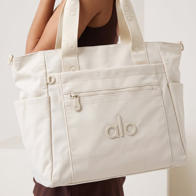 Cream Alo Yoga tote with branded webbing handles and front zip pocket