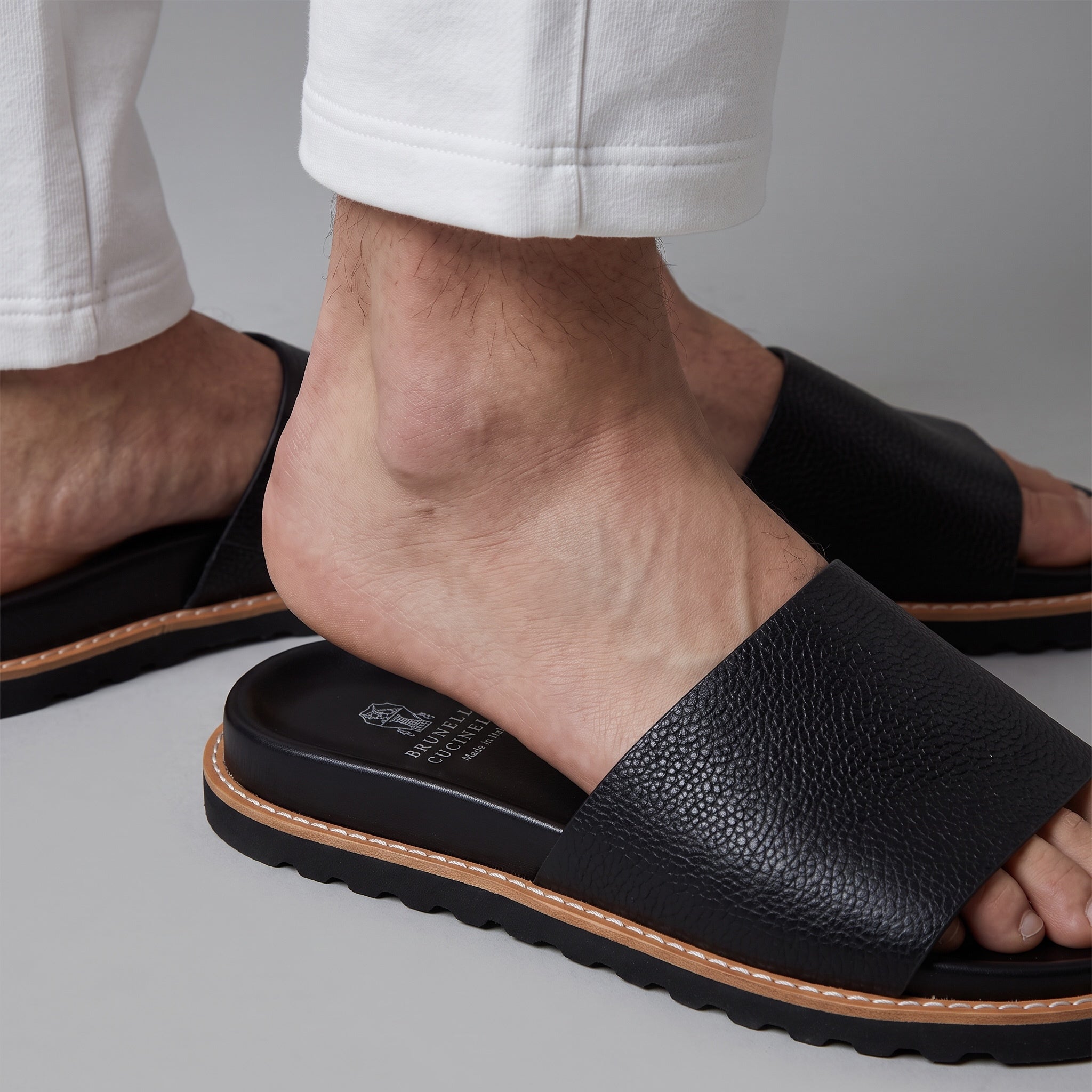 Brunello Cucinelli black pebbled single-strap sandals with stitched welt and printed footbed logo