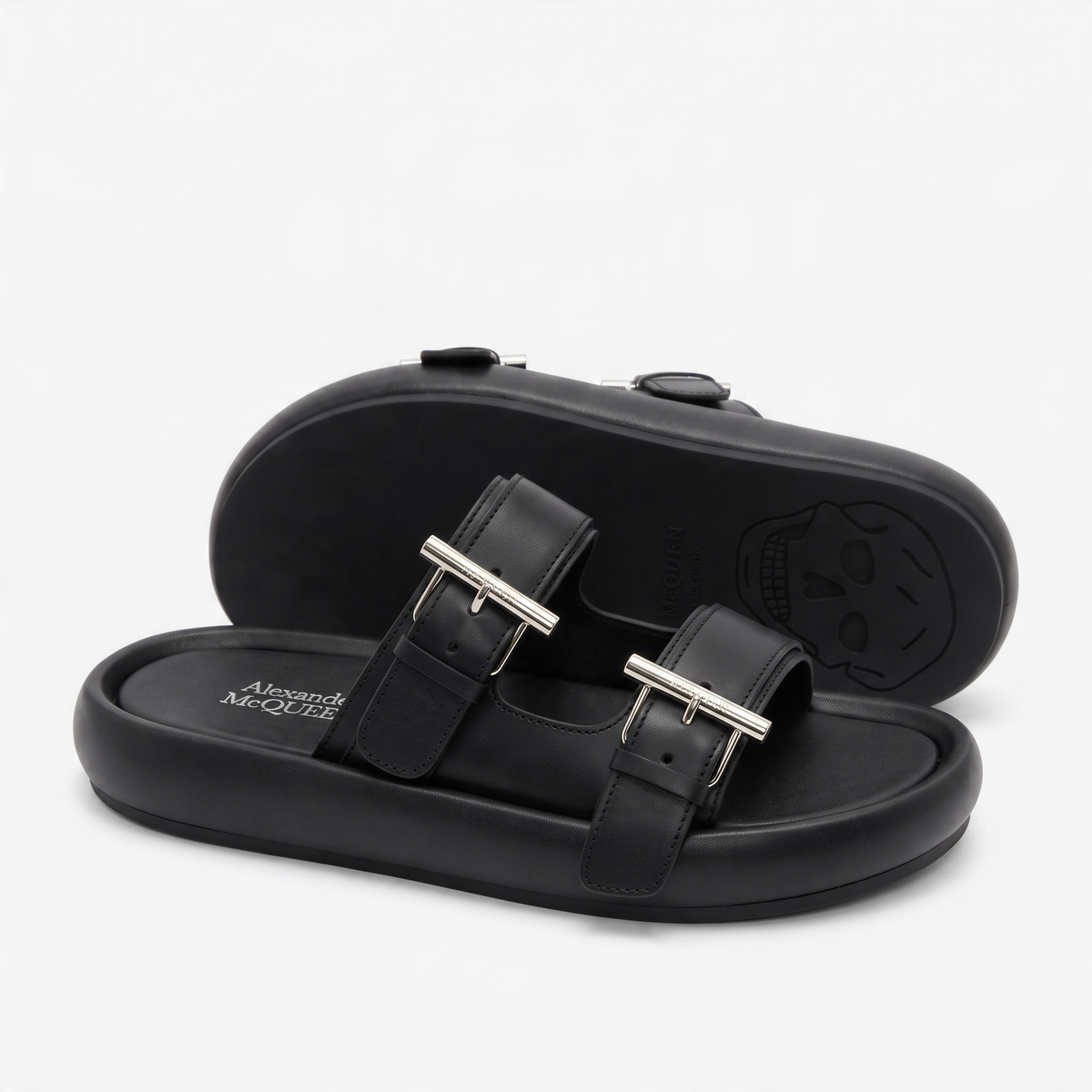 Pair of black Alexander McQueen double-strap slide sandals with metal buckles and skull embossed sole