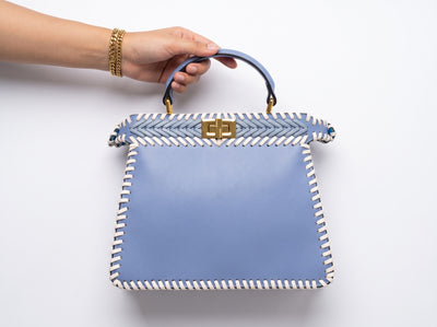 Light blue woven top-handle bag with white whipstitch trim and gold turn-lock clasp