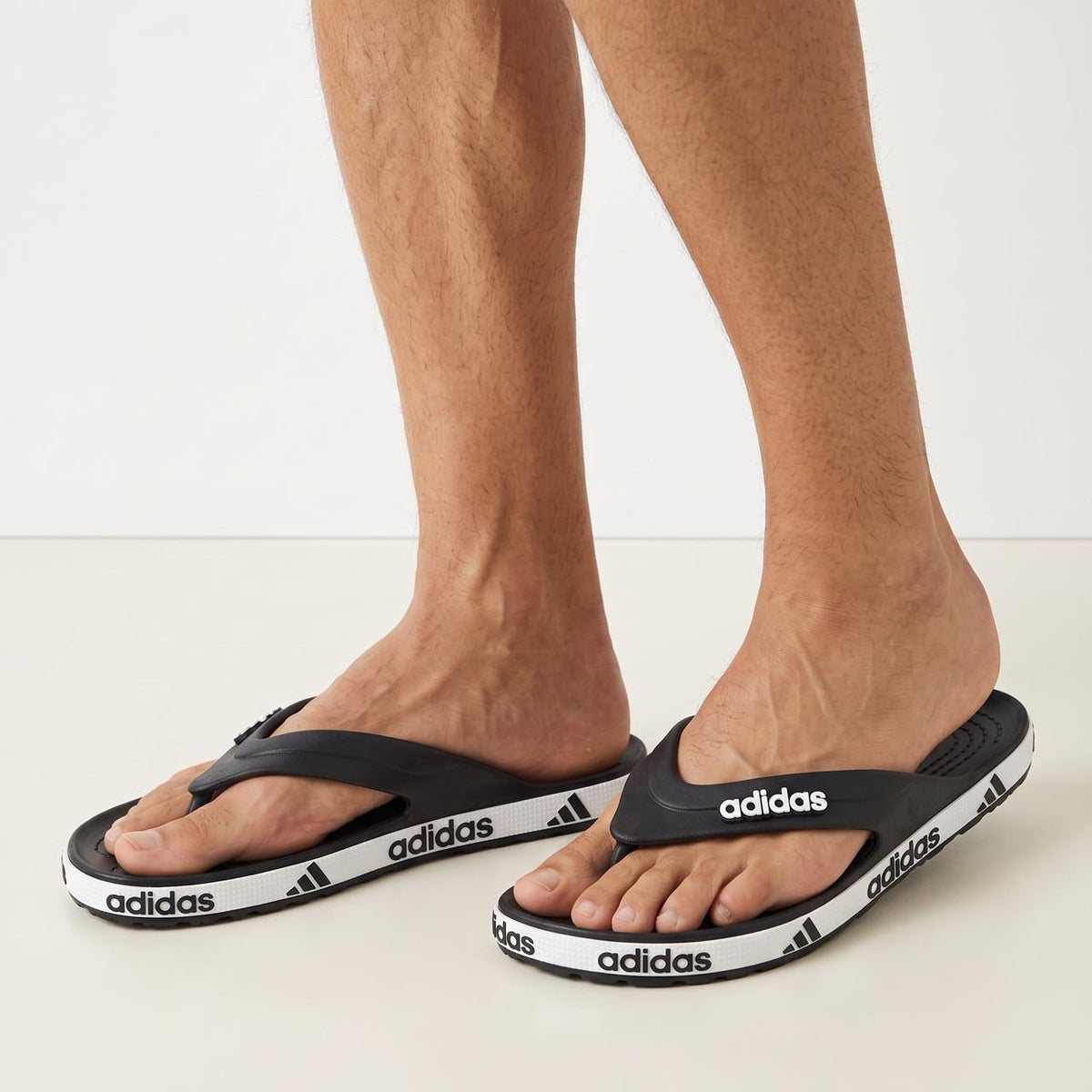 black adidas flip-flops with white adidas logo on strap and repeated logo on white midsole