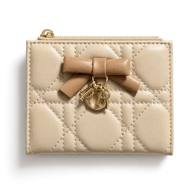 Beige Dior quilted compact wallet with bow and gold charm, open showing card slots and zip