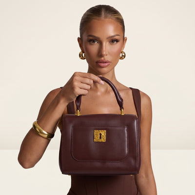 Burgundy top-handle bag with gold decorative hardware and front pocket