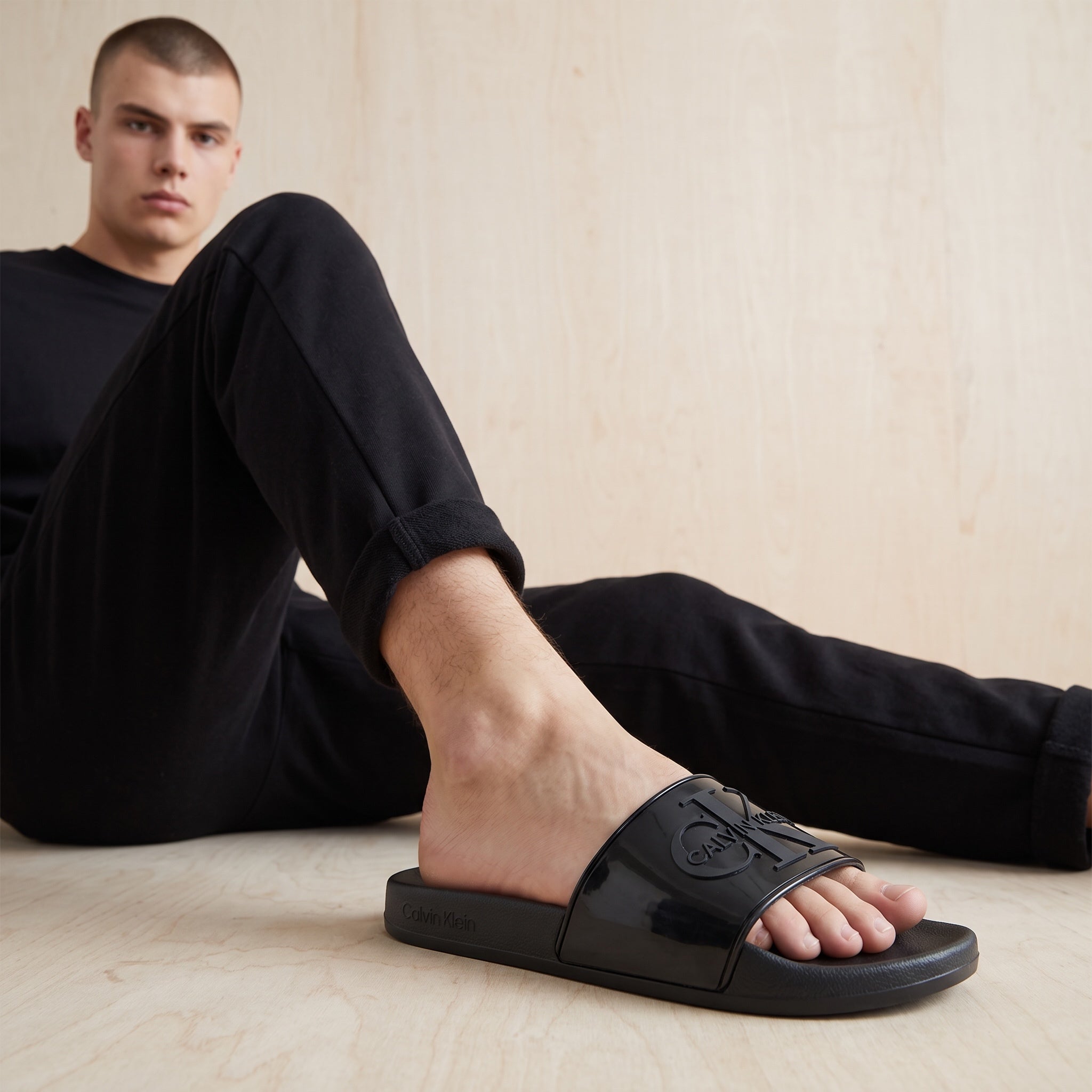 Black Calvin Klein slides with embossed logo on glossy strap worn by model