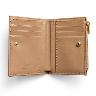 Beige Dior quilted compact wallet with bow and gold charm, open showing card slots and zip