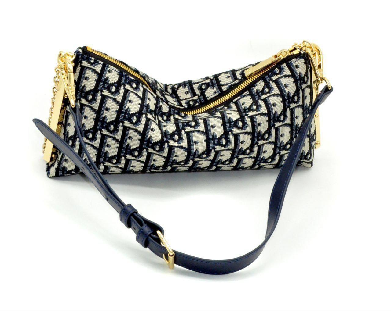 This exquisite Dior shoulder bag features the signature oblique jacquard pattern in navy and cream, a timeless symbol of the brand’s elegance. The gold-tone zipper and chain detailing add a luxurious touch, while the adjustable leather strap ensures both