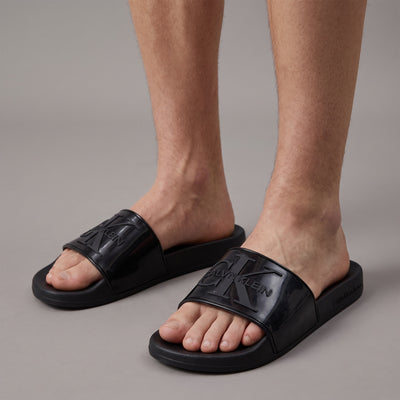 Black Calvin Klein slides with embossed logo on glossy strap worn by model