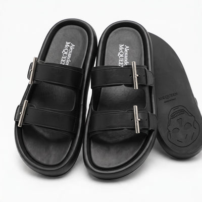 Pair of black Alexander McQueen double-strap slide sandals with metal buckles and skull embossed sole