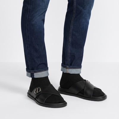 Black Dior crisscross slide sandal with metal CD logo and textured rubber sole, shown on model feet