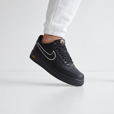 black Nike Air Force 1 low-top sneaker with white outline swoosh and yellow accents