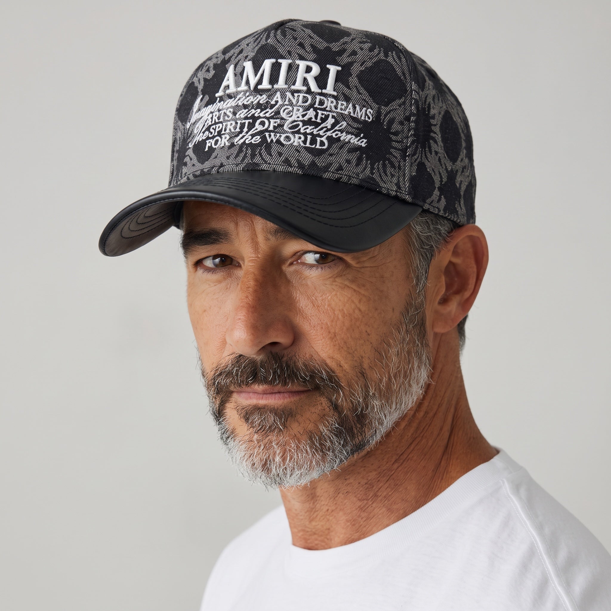 Man wearing a black Amiri trucker cap with grey paisley print and embroidered logo