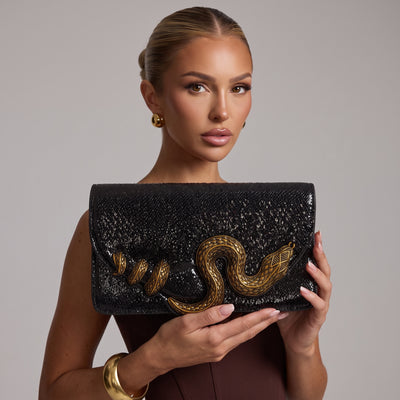 Black glossy clutch with large gold snake applique held by model