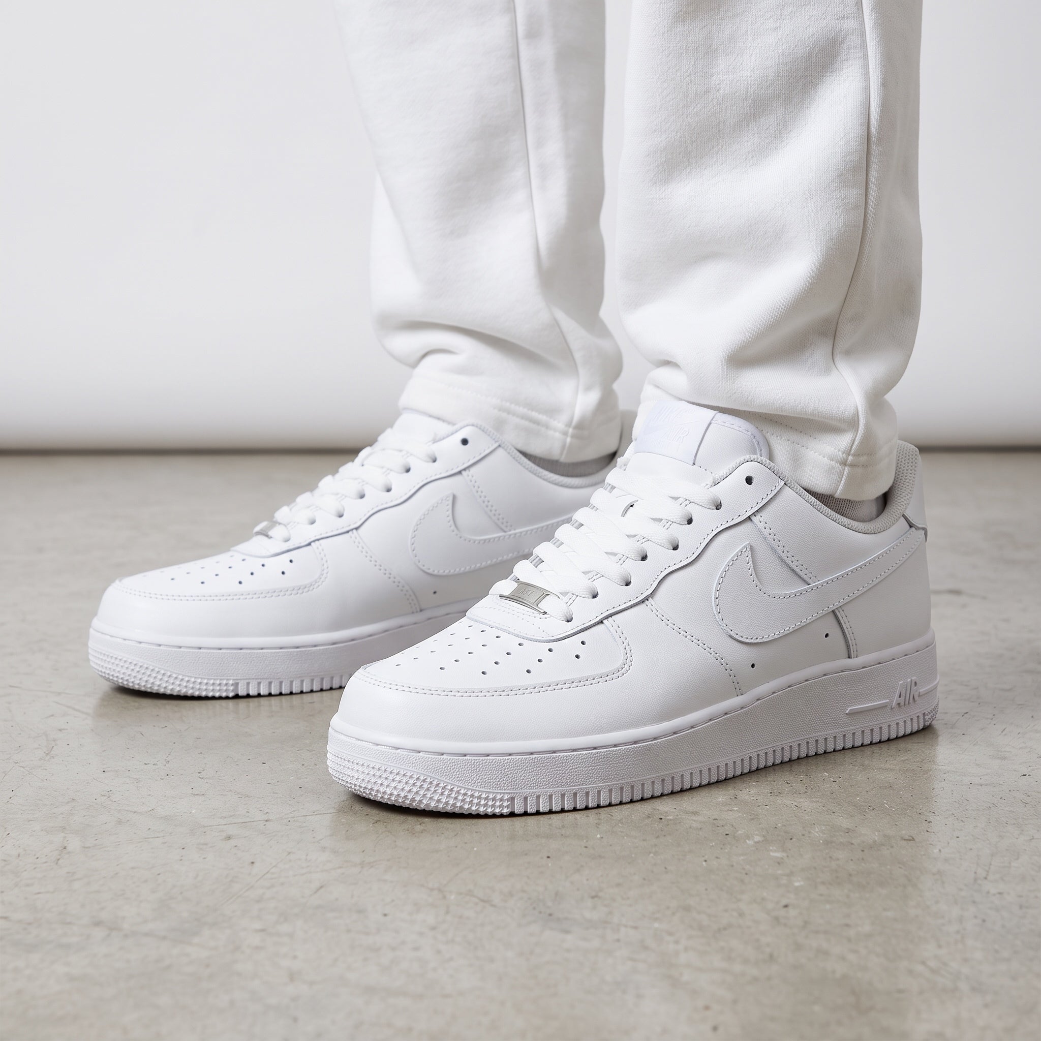 Pair of Nike Air Force 1 Low triple white sneakers on concrete floor