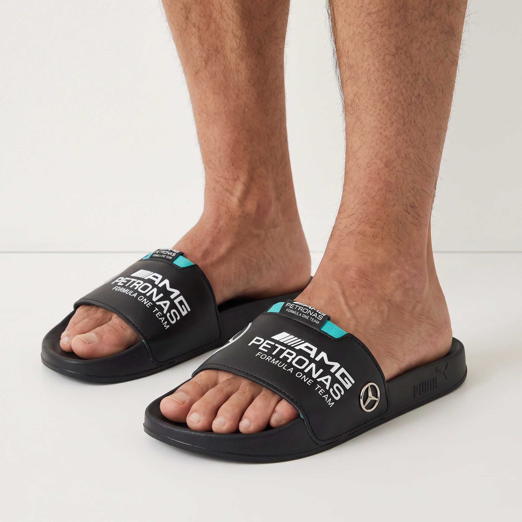 black Puma Mercedes‑AMG Petronas logo slides with turquoise trim on model feet