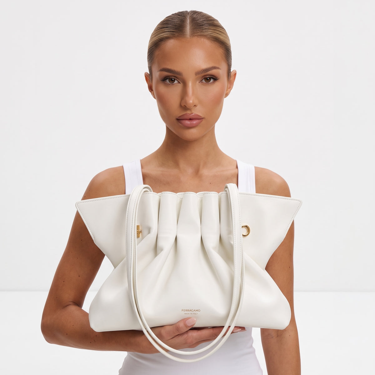 White Ferragamo ruched tote bag with gold hardware held on model shoulder