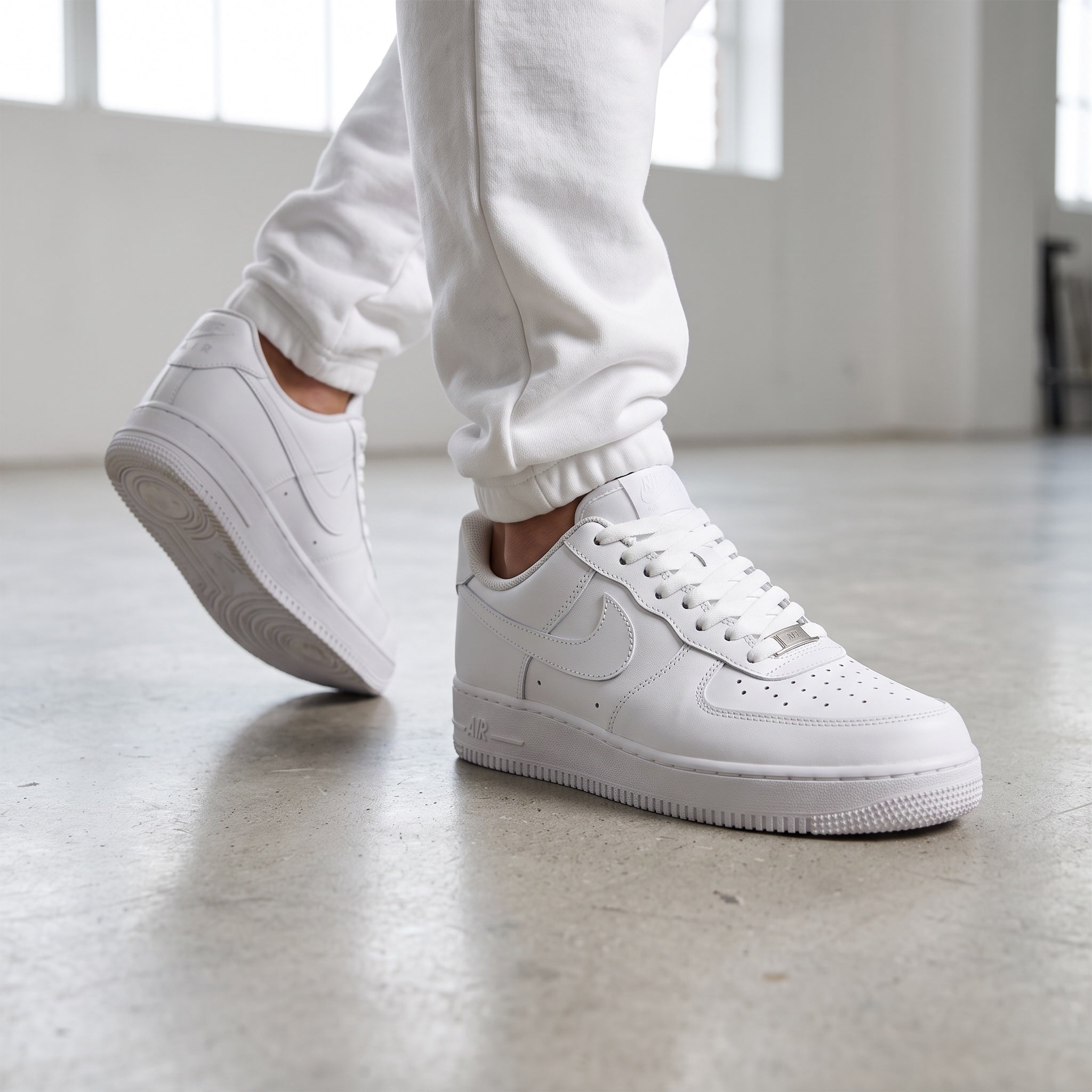 Pair of Nike Air Force 1 Low triple white sneakers on concrete floor