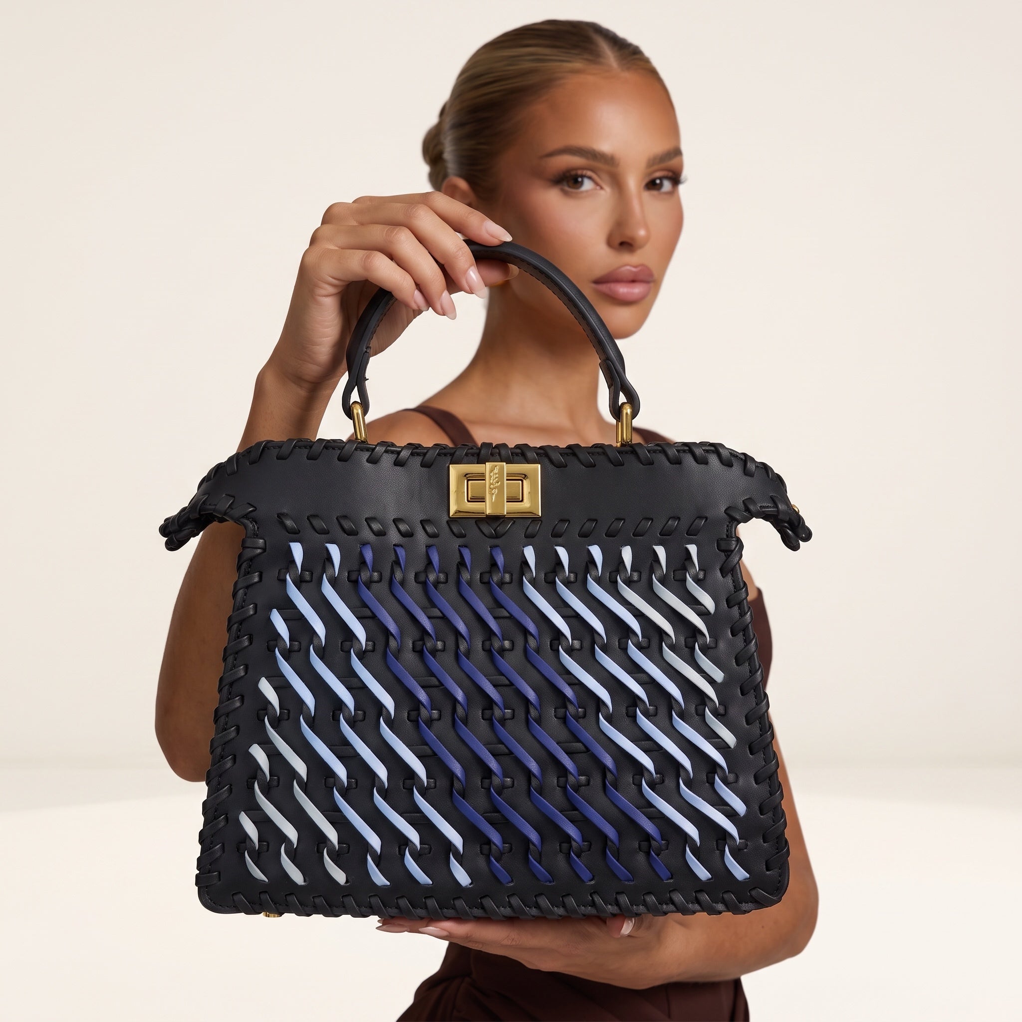 black top-handle bag with blue woven ribbon accents and gold rectangular clasp