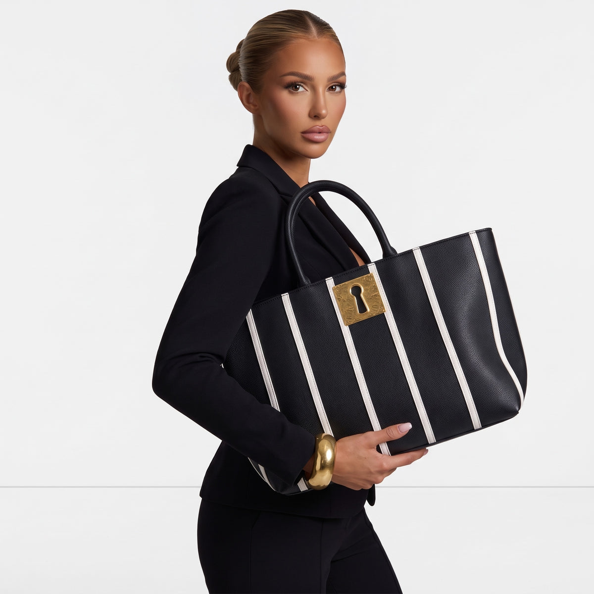 Black tote bag with vertical white stripes and gold keyhole plaque