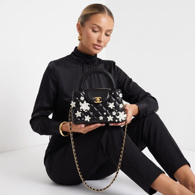 black quilted mini top-handle bag with white floral and pearl appliqués and gold chain strap