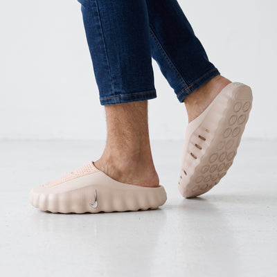 Blush pink one-piece Nike foam clogs with silver swoosh, slip-on style