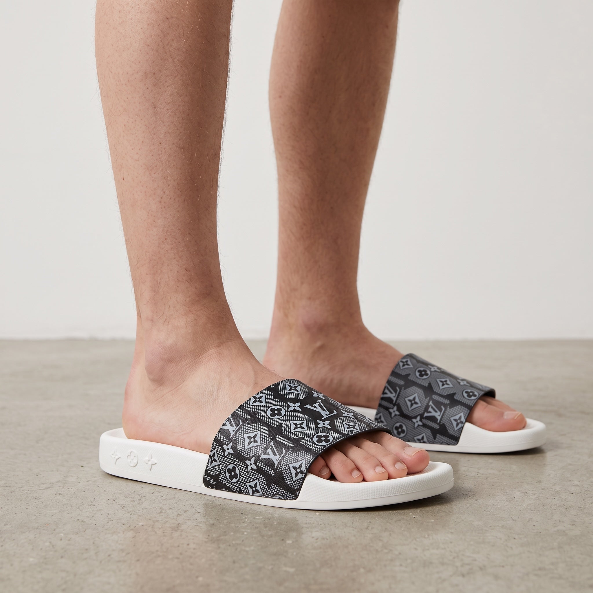 Close-up of men's feet wearing Louis Vuitton black monogram slide sandals with white sole