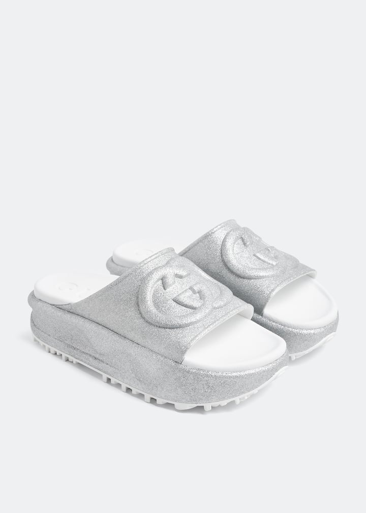 Silver Gucci flatform slides with glitter finish and raised interlocking G logo on white footbed