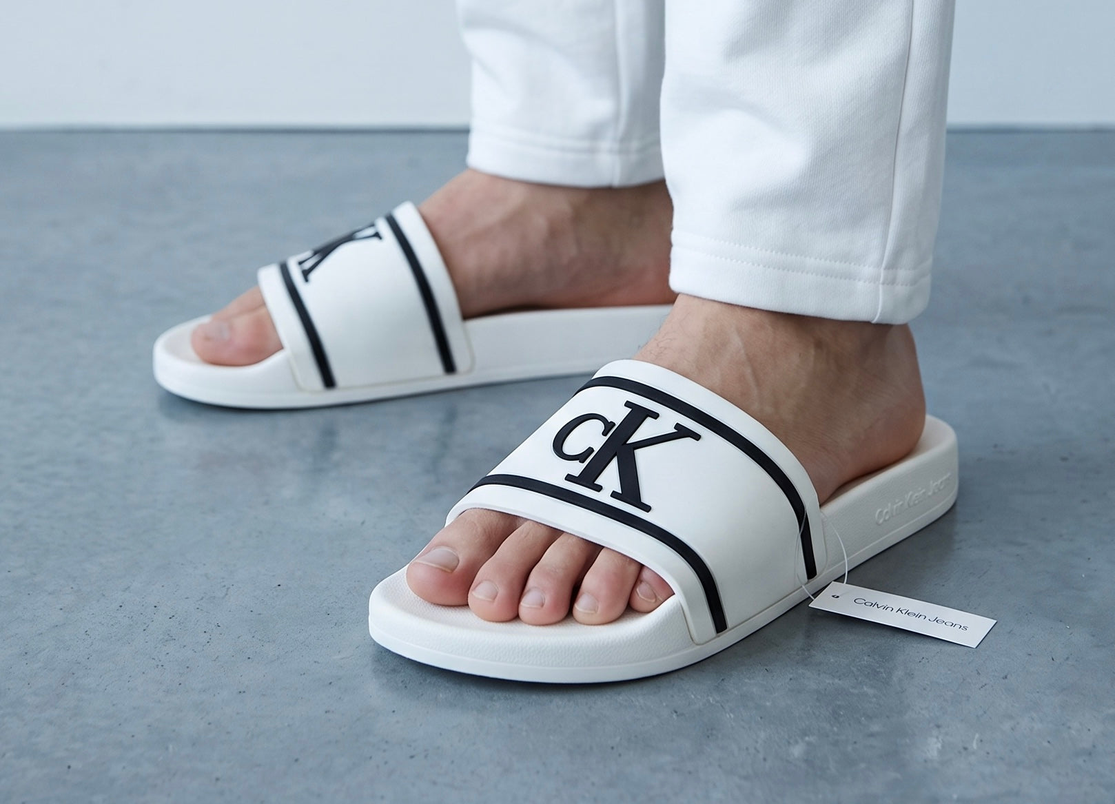 White Calvin Klein slides with black CK logo on wide strap, worn on feet