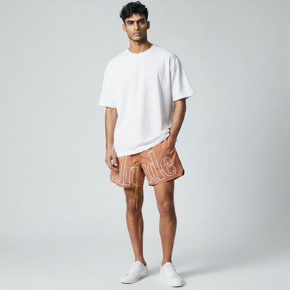 MASTERPIECE brown quick-dry swim shorts with oversized white Rhude logo and yellow drawstring.