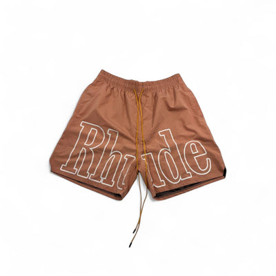 MASTERPIECE brown swim shorts with oversized white Rhude logo, elastic waist, and yellow drawstring.
