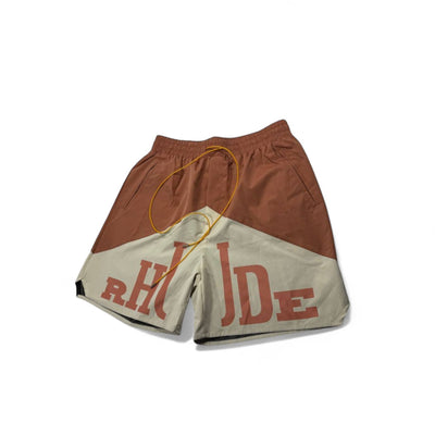 MASTERPIECE Rhude panel shorts in rust brown and cream with oversized RHUDE branding and yellow drawstring. Lightweight, fast-drying fabric.