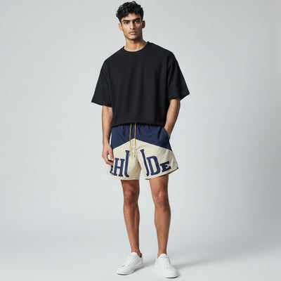 MASTERPIECE navy and cream Rhude swim shorts with oversized logo and yellow drawstring. Lightweight, fast-drying summer essential.